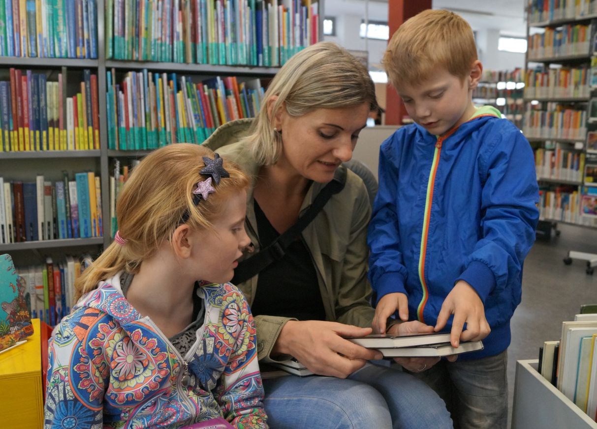 Eine Frau und zwei Kinder suchen in der Bücherei ein Buch aus